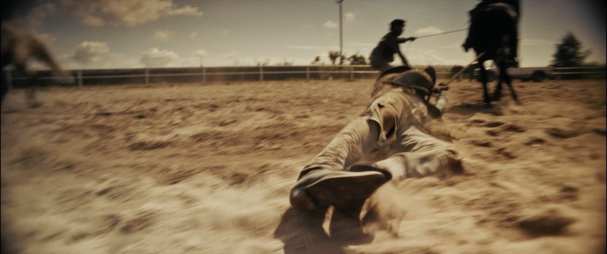 Motion-blurred rodeo action - a figure dragged across a dusty arena on a rope, riders behind - Amon Amarth